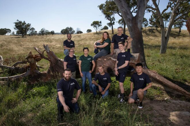 wildlife drones careers - a group of people wearing navy and green shirts they are standing in grass and some are sitting on a large fallen tree