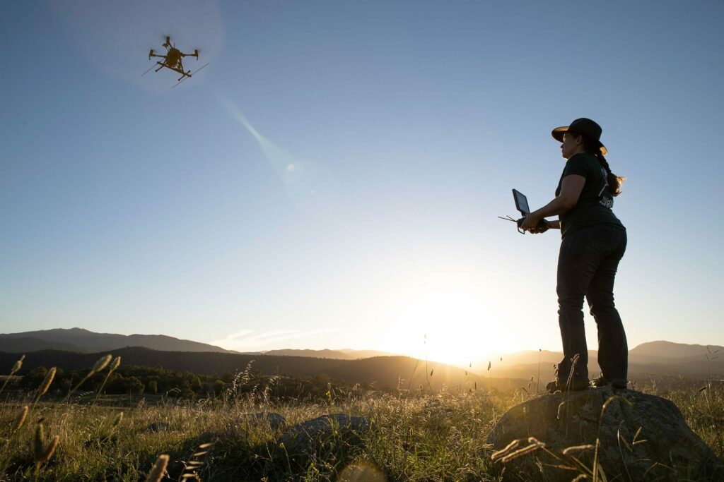 a silhouette of a woman standing on a rock looking at a drone in the air
