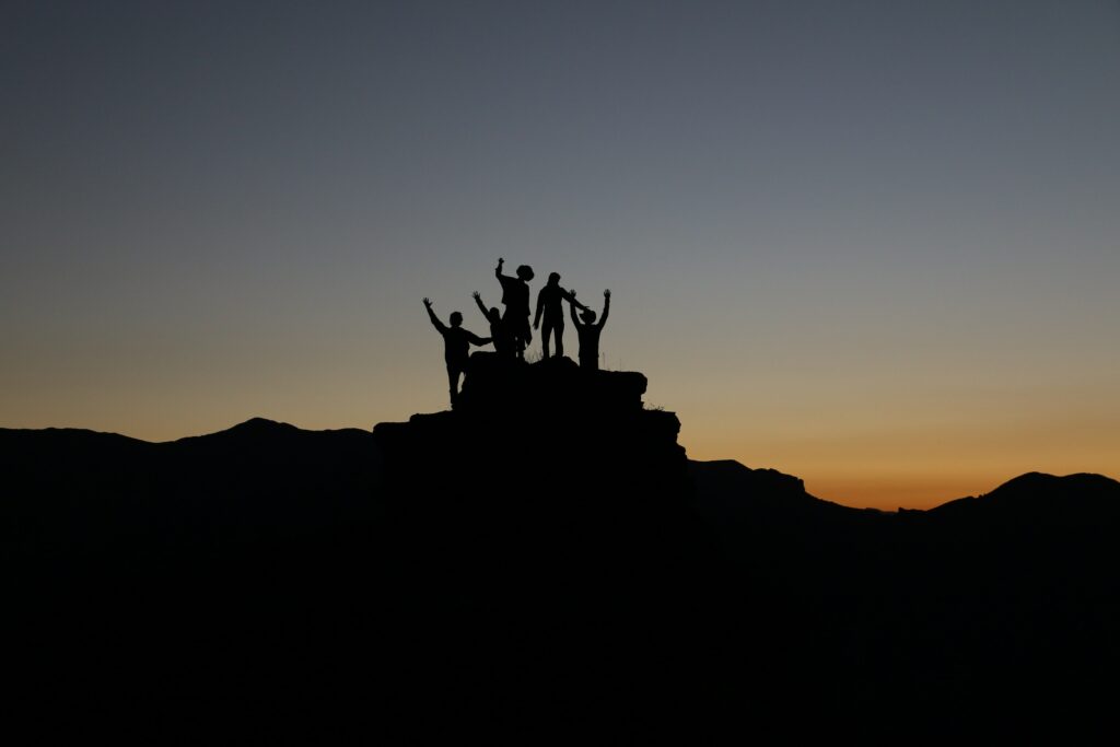 silhouette of a group of people standing on top of a rock at sunset